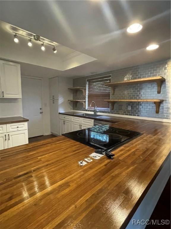 kitchen with black electric cooktop, sink, white cabinets, and butcher block countertops