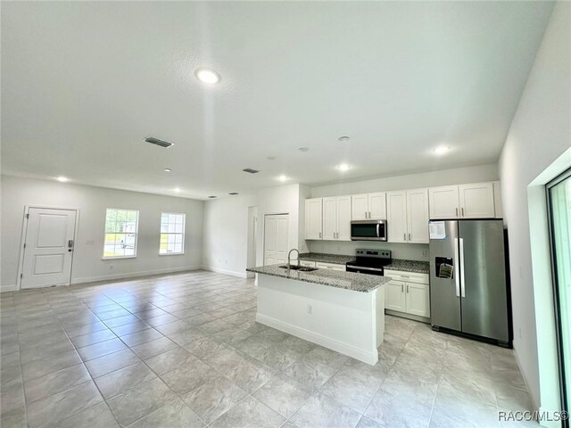 kitchen featuring white cabinetry, a center island with sink, stainless steel appliances, and light stone counters