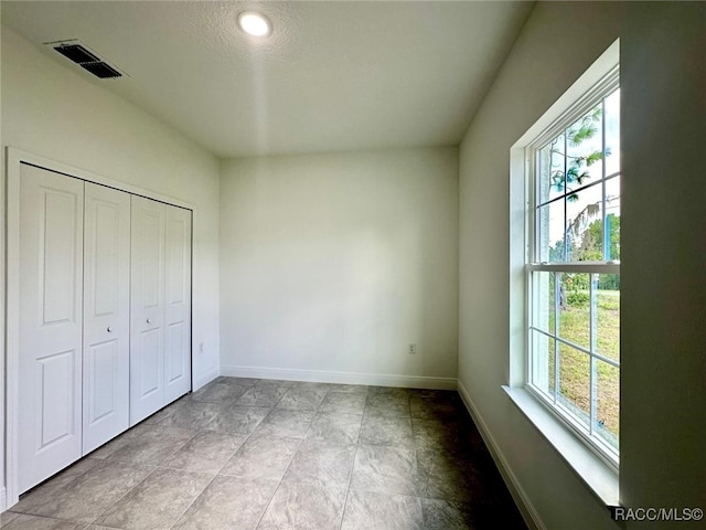 unfurnished bedroom featuring multiple windows, a closet, and a textured ceiling