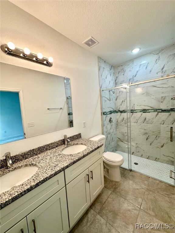 bathroom with vanity, tile patterned floors, toilet, a textured ceiling, and walk in shower