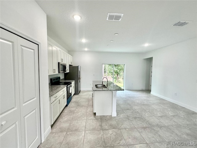 kitchen featuring appliances with stainless steel finishes, a center island with sink, white cabinetry, and dark stone counters