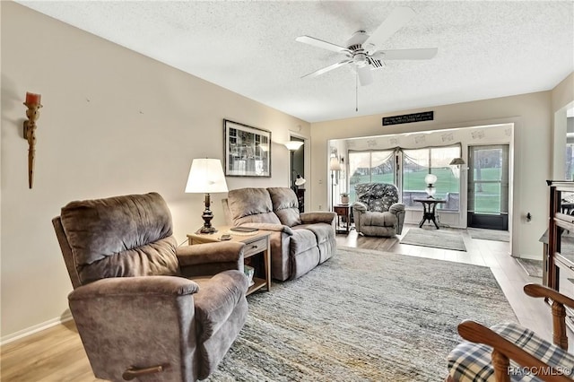 living area with a textured ceiling, baseboards, a ceiling fan, and light wood-style floors