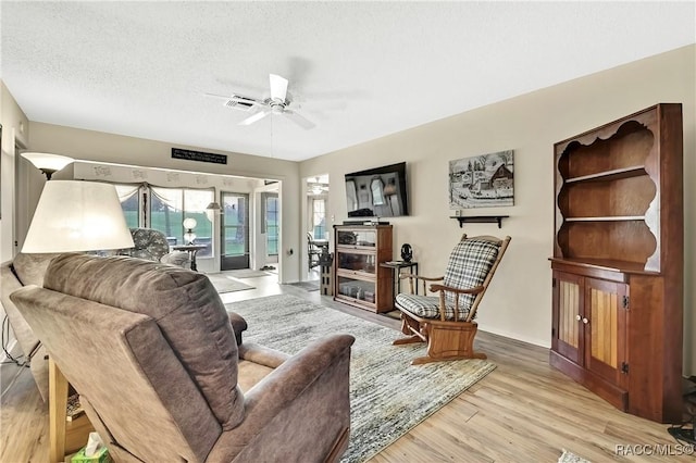 living room featuring a textured ceiling, light wood finished floors, visible vents, and a ceiling fan