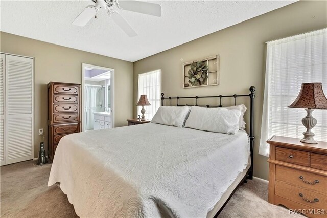 bedroom with a closet, light colored carpet, a ceiling fan, a textured ceiling, and ensuite bath