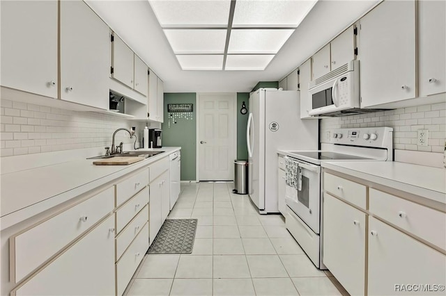 kitchen with white appliances, light countertops, white cabinetry, a sink, and light tile patterned flooring