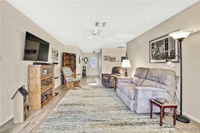 living room with light wood-type flooring, ceiling fan, visible vents, and baseboards