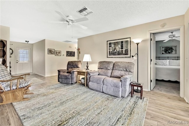 living room featuring a ceiling fan, visible vents, light wood-style flooring, and a textured ceiling