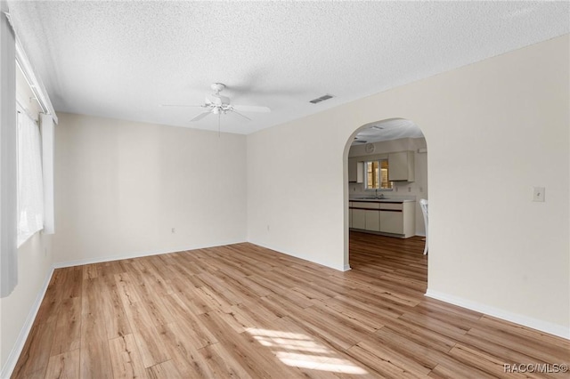 unfurnished room with ceiling fan, sink, a textured ceiling, and light wood-type flooring