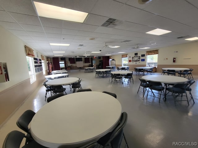 dining space featuring a wealth of natural light, ceiling fan, a drop ceiling, and concrete flooring