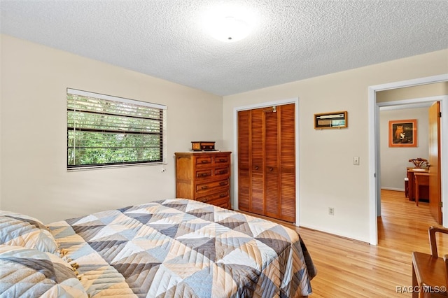 bedroom with light wood-type flooring, a textured ceiling, and a closet