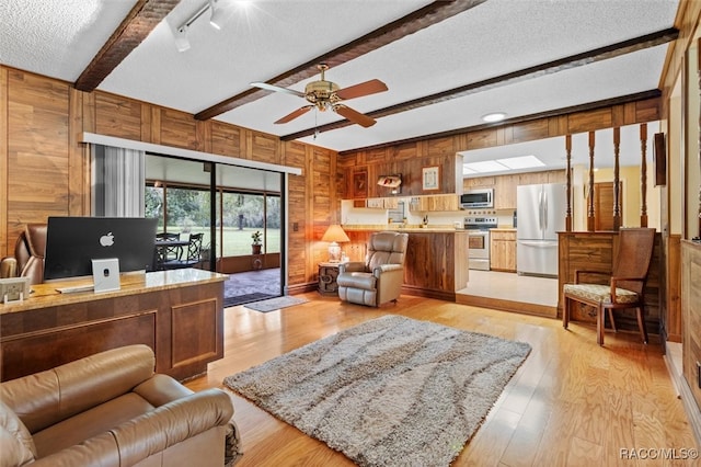 living room with wooden walls, light wood-type flooring, ceiling fan, a textured ceiling, and beam ceiling