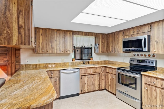 kitchen featuring a skylight, sink, stainless steel appliances, decorative backsplash, and light tile patterned floors