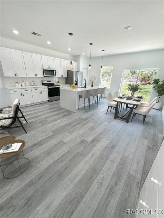 kitchen featuring appliances with stainless steel finishes, pendant lighting, an island with sink, white cabinets, and light hardwood / wood-style flooring