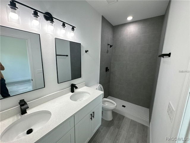 bathroom featuring hardwood / wood-style flooring, vanity, tiled shower, and toilet