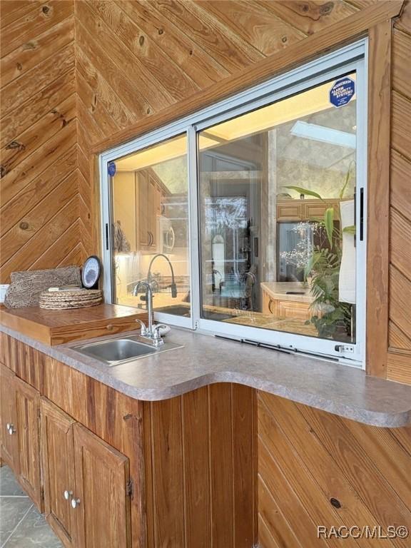 bar with light tile patterned floors, sink, wood walls, and wooden ceiling