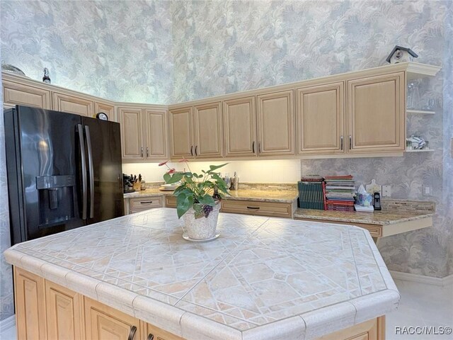 kitchen with black fridge, light brown cabinetry, a kitchen island, and tile countertops