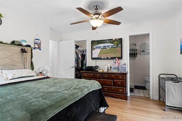 bedroom with a textured ceiling, light wood-type flooring, ensuite bathroom, and ceiling fan