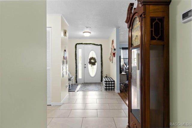 entrance foyer featuring light tile patterned floors, a textured ceiling, and ornamental molding