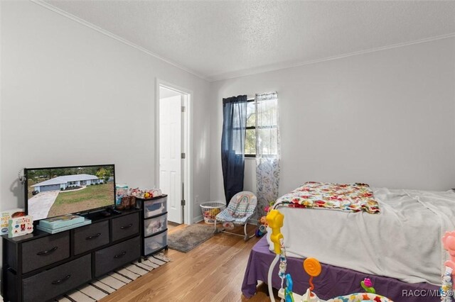 bedroom featuring light hardwood / wood-style flooring, a textured ceiling, and ornamental molding