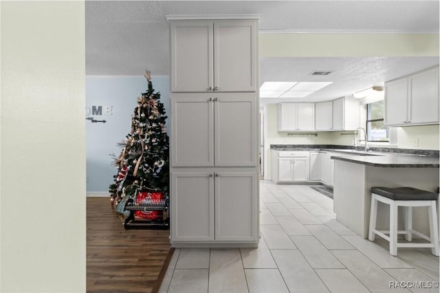 kitchen with white cabinetry, sink, a textured ceiling, a breakfast bar, and ornamental molding