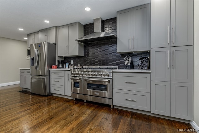 kitchen featuring appliances with stainless steel finishes, backsplash, wall chimney range hood, gray cabinets, and dark hardwood / wood-style floors