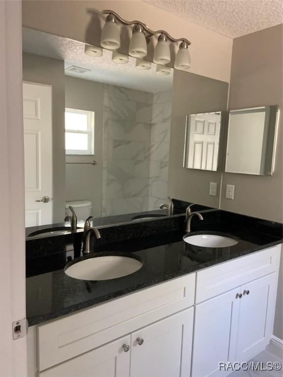 bathroom with vanity, toilet, a textured ceiling, and a tile shower