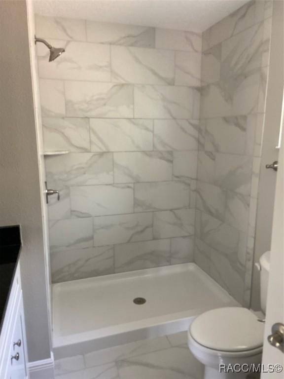 bathroom with tiled shower, vanity, and toilet