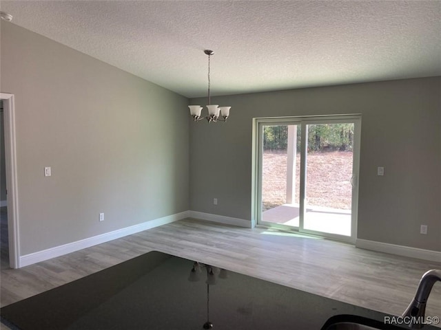 unfurnished dining area with hardwood / wood-style floors, a notable chandelier, and a textured ceiling