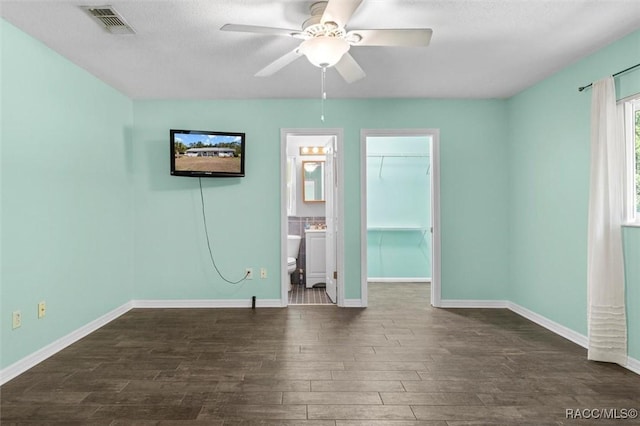 unfurnished bedroom with baseboards, visible vents, dark wood finished floors, ensuite bath, and a walk in closet