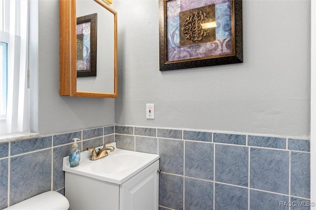 bathroom with a wainscoted wall, toilet, tile walls, and vanity