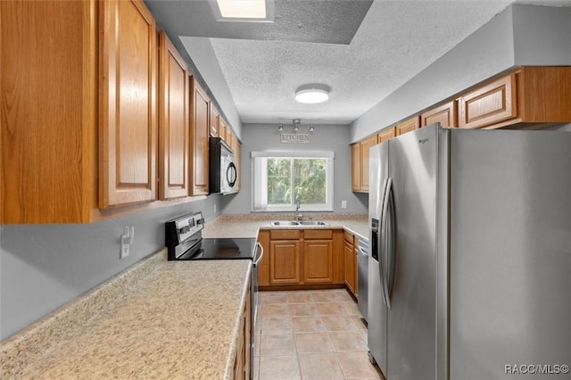 kitchen with a sink, a textured ceiling, stainless steel appliances, brown cabinetry, and light countertops