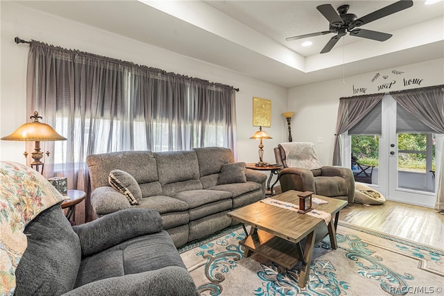 living room featuring hardwood / wood-style floors, ceiling fan, a raised ceiling, and french doors