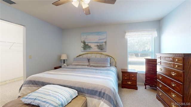 bedroom featuring a walk in closet, light carpet, a closet, and ceiling fan