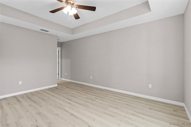 spare room featuring light hardwood / wood-style floors, ceiling fan, and a raised ceiling