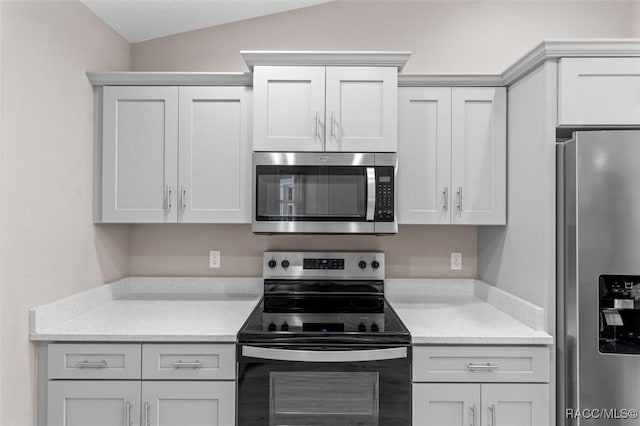 kitchen with white cabinets, stainless steel appliances, light stone counters, and lofted ceiling