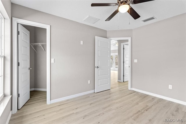 unfurnished bedroom with a walk in closet, a closet, ceiling fan, and light hardwood / wood-style flooring