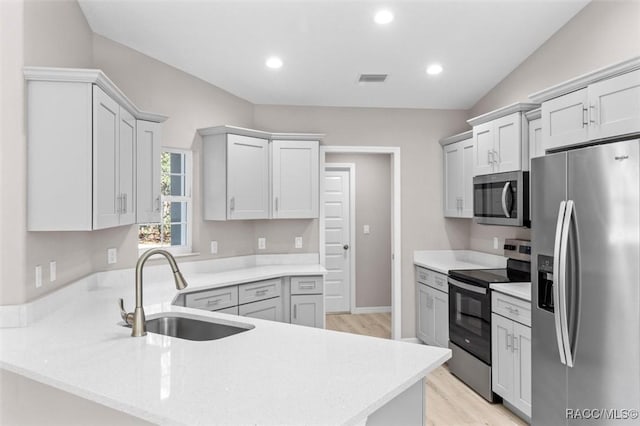 kitchen with stainless steel appliances, sink, vaulted ceiling, and light wood-type flooring