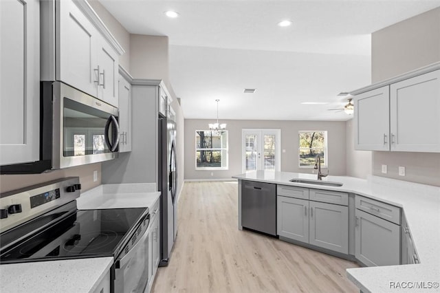 kitchen with kitchen peninsula, light hardwood / wood-style flooring, ceiling fan with notable chandelier, appliances with stainless steel finishes, and sink