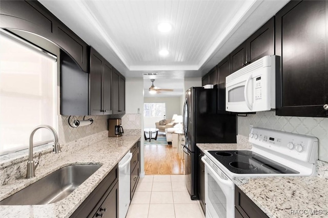 kitchen featuring white appliances, sink, ceiling fan, a tray ceiling, and light stone counters