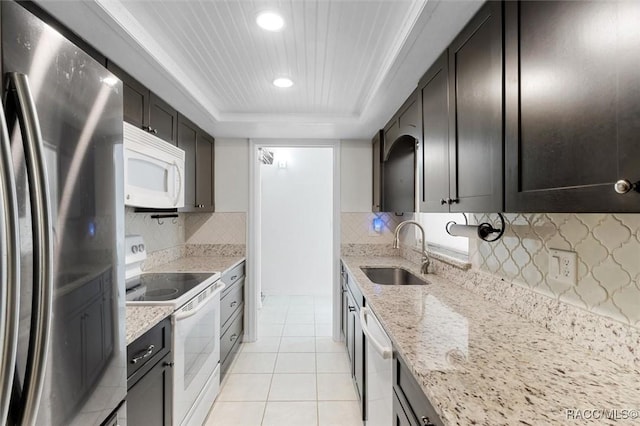 kitchen with decorative backsplash, light stone counters, stainless steel appliances, a raised ceiling, and sink