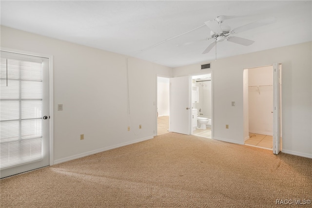 unfurnished bedroom featuring light carpet, ensuite bathroom, ceiling fan, a spacious closet, and a closet