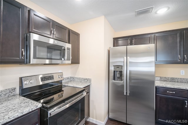 kitchen featuring appliances with stainless steel finishes, dark brown cabinetry, and light stone counters