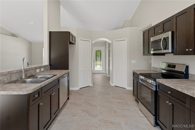 kitchen featuring dark brown cabinetry, stainless steel appliances, vaulted ceiling, and sink