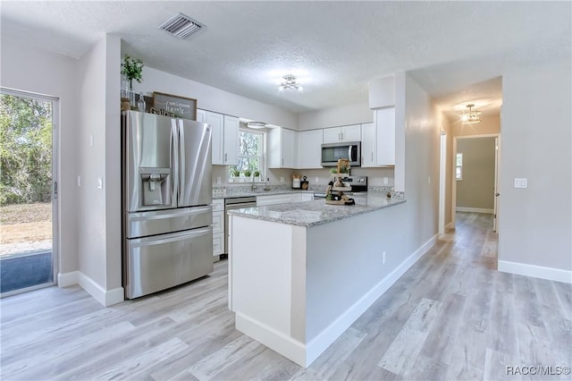 kitchen featuring a textured ceiling, appliances with stainless steel finishes, a peninsula, white cabinetry, and visible vents