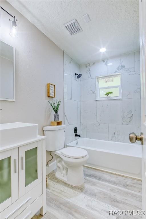 full bath featuring a textured ceiling,  shower combination, toilet, visible vents, and wood finished floors