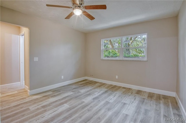 spare room featuring light wood finished floors, a ceiling fan, and baseboards