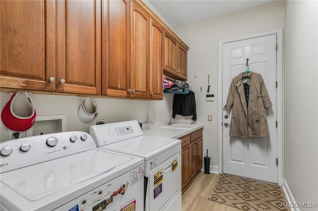 laundry room with light wood-type flooring, a sink, washing machine and dryer, cabinet space, and baseboards