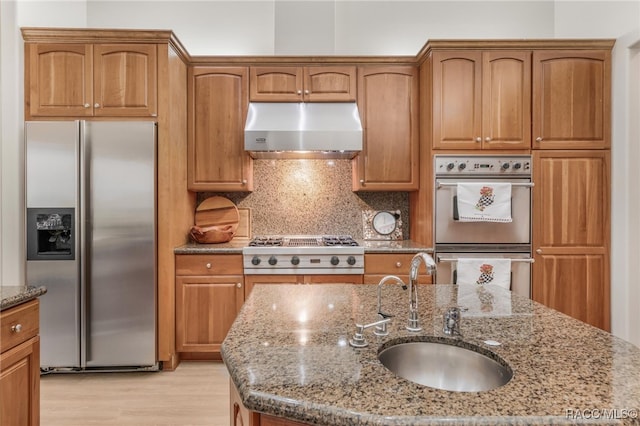 kitchen featuring under cabinet range hood, a sink, stainless steel appliances, decorative backsplash, and light stone countertops