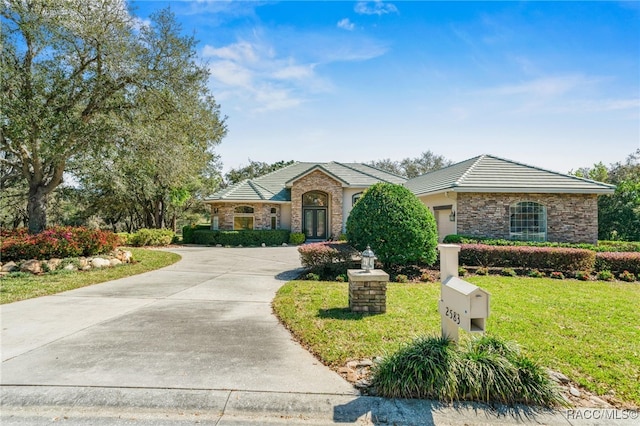 view of front of home with a tile roof, a front yard, driveway, stone siding, and an attached garage