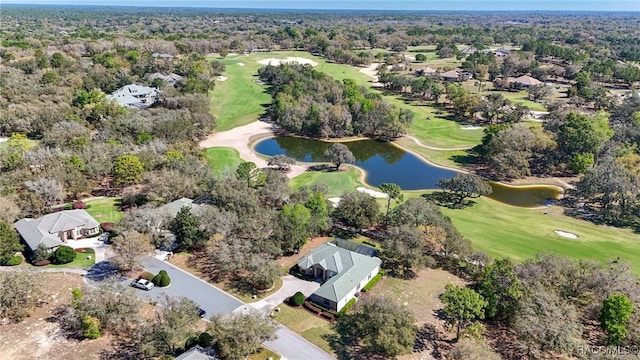 drone / aerial view with view of golf course, a view of trees, and a water view